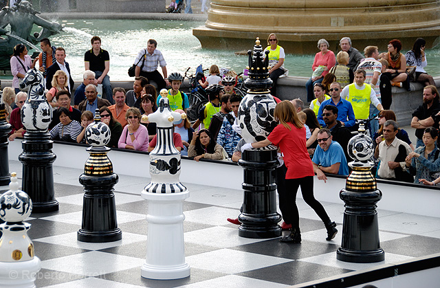 Woman moving a giant chess piece during a game in Trafalgar Square, London, England. The Tournament, an installation created by Spanish designer, Jaime Hayón consists of a gigantic chess set, with 2m high ceramic pieces designed by Hayón on a specially cr