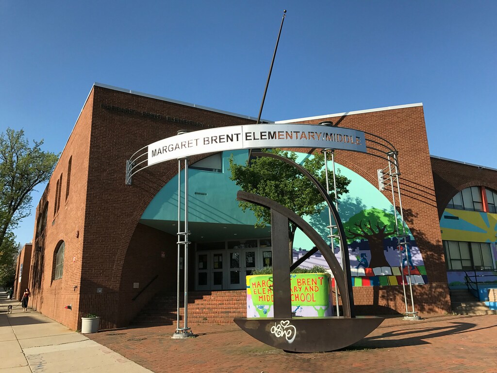 The corner of a brick school building with a metal sign and metal modernist sculpture in the foreground.