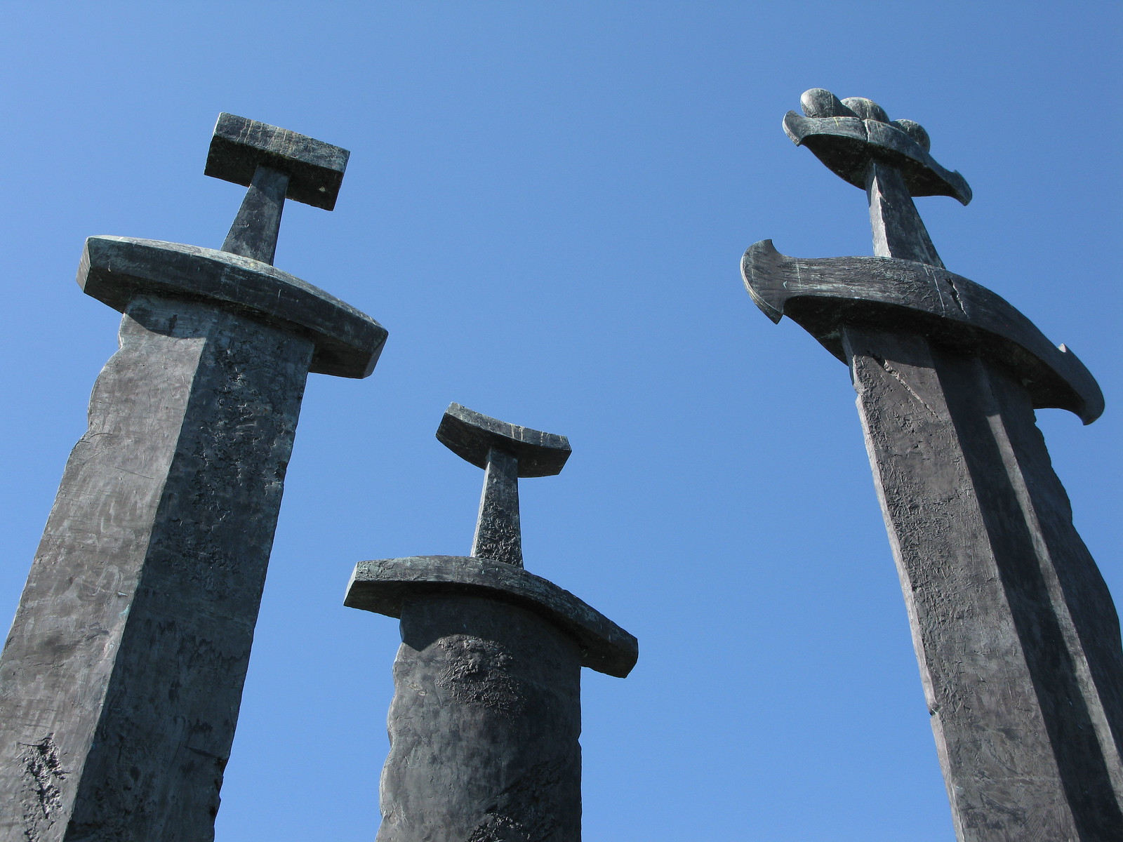 The handles of three gigantic sword statues seen against a blue sky