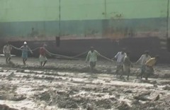 Barefoot workers hauling metal in the mud