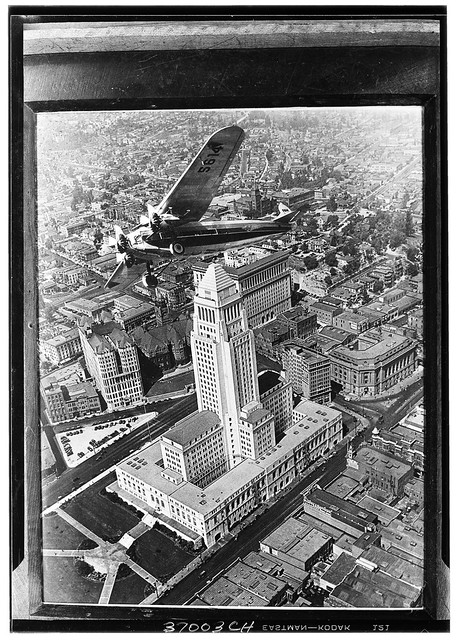 Ford Tri-motor airplane flying over Los Angeles City Hall 1929