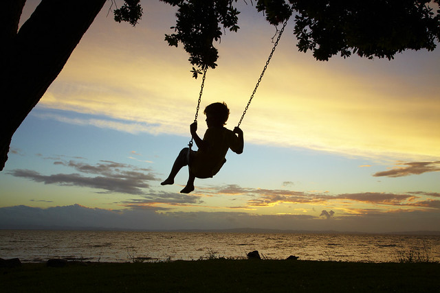 Young Boy on Rope Swing under Pohutukawa Tree at Sunset, Thames, Coromandel, North Island, New Zealand