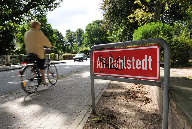 7075 Ortsteilschild Alt Rahlstedt -  Fahrradfahrerin auf dem Gehweg der Oldenfelder Strasse.