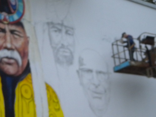 Painter on a lift beside a partly coloured portrait mural