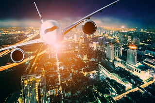 Airplane for transportation flying over the city at night scene, city on beautiful sunset background