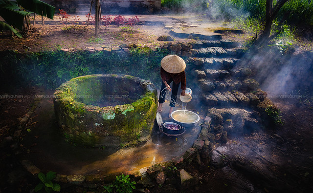 The older woman scoop water from water well in Son Tay district, Vietnam