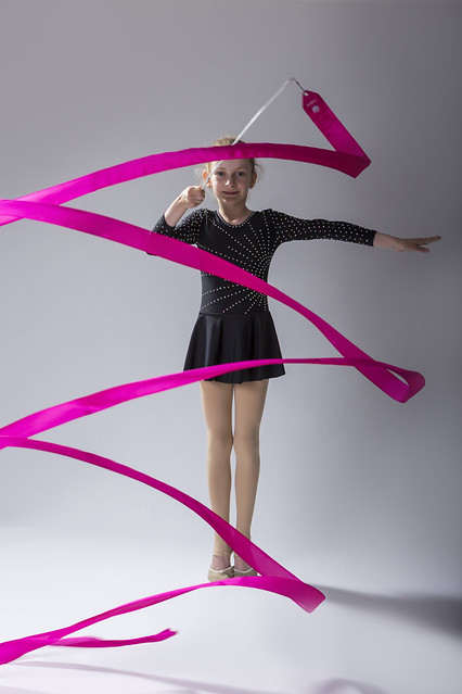 High Contrsat Portrait of Caucasian Female Rhythmic Gymnast In Professional Competitive Black Sparkling Starry Suit Doing Artistic Ribbon Spirals Exercises in Studio.
