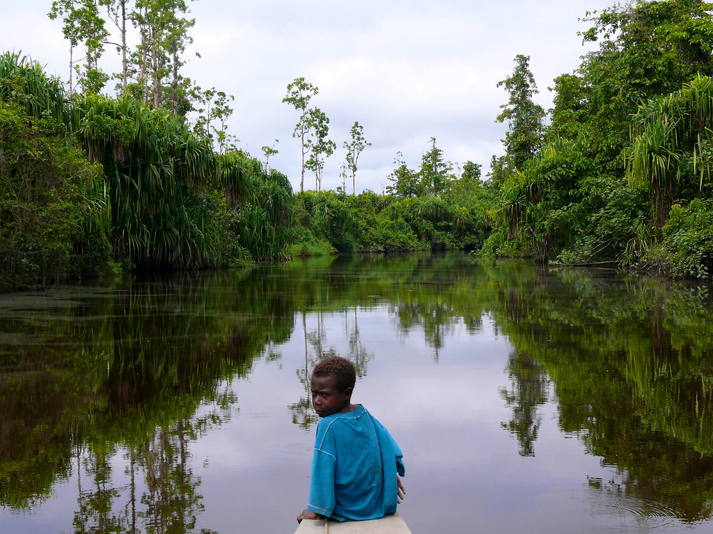 A boy, sitting on the edge of the boat, looks back as we go down the river, Papua, Indonesia.