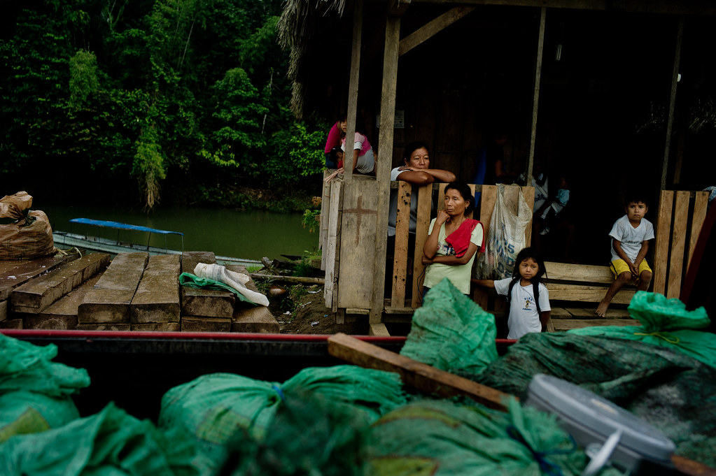 Kichwa villagers sit next to timber on the banks of the Puni River during the Friday markets, Napo Province, Ecuador.