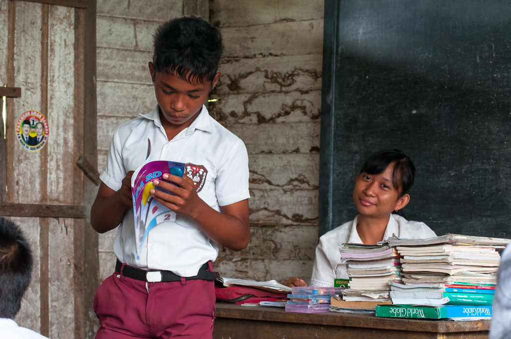 A 3rd grade student in Pengerak village is reading a tutorial book in front of the class, West Kalimantan, Indonesia.