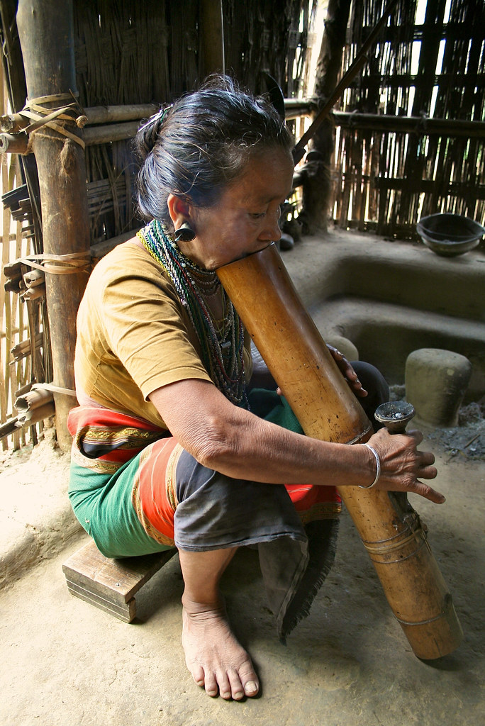 A woman smoking through a bamboo pipe. Bangladesh.