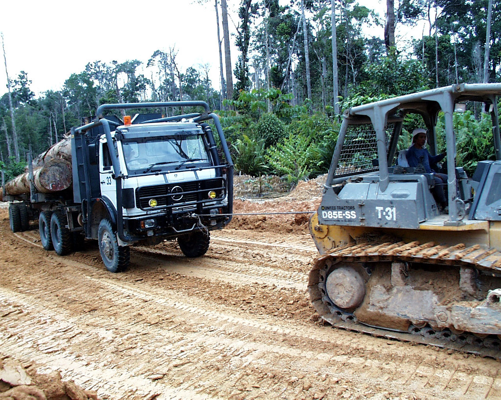 A bulldozer helps a logging truck gain traction on the muddy road, Indonesia.