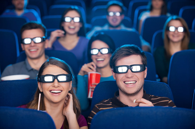Watching three-dimensional movie. Happy young people in three-dimensional glasses watching movie at the cinema together