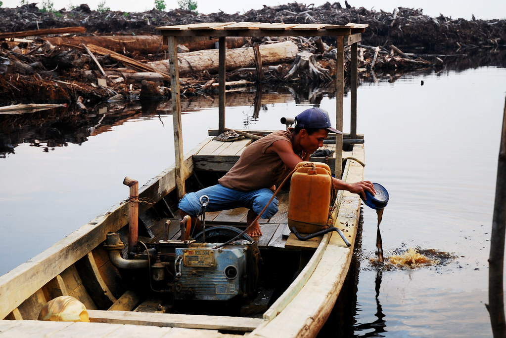 A man clearing up his boat on a water way on peatland area. Indonesia. Land clearing on peatland in Indonesia.