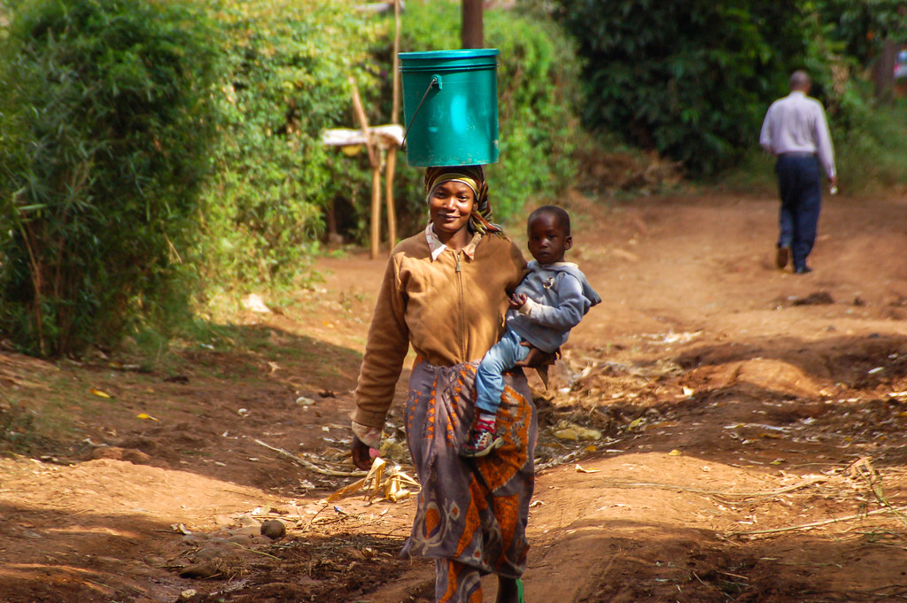 A woman balancing water and carrying her child. Tanzania.
