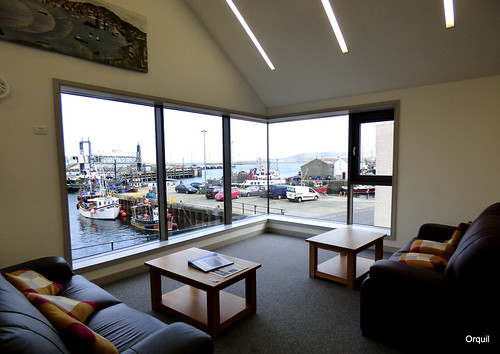 stromness library new building firstfloor readingarea bigwindow waterfront adjacentharbour view outlook piers elevated pedestrianwalkway boats fishingboats smallferry parkedvehicles harbourbuildings modern interior sofas smalltables carpet modernroom stromnessharbour westmainland orkney islands august evening summer calm seawater ripples scotland uk unitedkingdom greatbritain britain orcades elevatedview viewpoint interesting unusual nice hamnavoeabscence