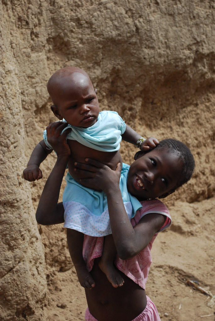 Elder sister holding her baby sister aloft, Africa.