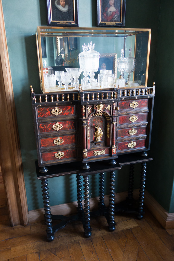Baroque cabinet with glass goblets. Moreover, the chest has dark, spiral legs and a deep red-painted chest with gold hardware.