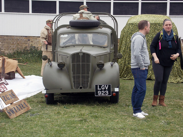 BRITISH ARMY SECOND WORLD WAR  1938 UTILITY OR  PICK UP TRUCK WITH SECOND WORLD WAR GERMAN UNIFORMED RE-ENACTORS AND A MAN AND WOMAN STANDING TALKING AT A VE DAY EVENT AT THE ROYAL GUNPOWDER MILLS IN AN EAST LONDON BOROUGH SUBURB STREET VENUE ENGLAND 0002