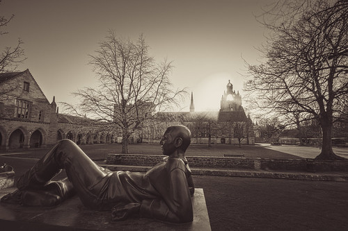 fine art black & white view of the reclining student bronze with King's College and chapel in front of winter sun. University of Aberdeen, Aberdeen, Scotland