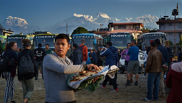 Nepali seller at tourist bus stop in front of Annapurna massif, Pokhara, Nepal