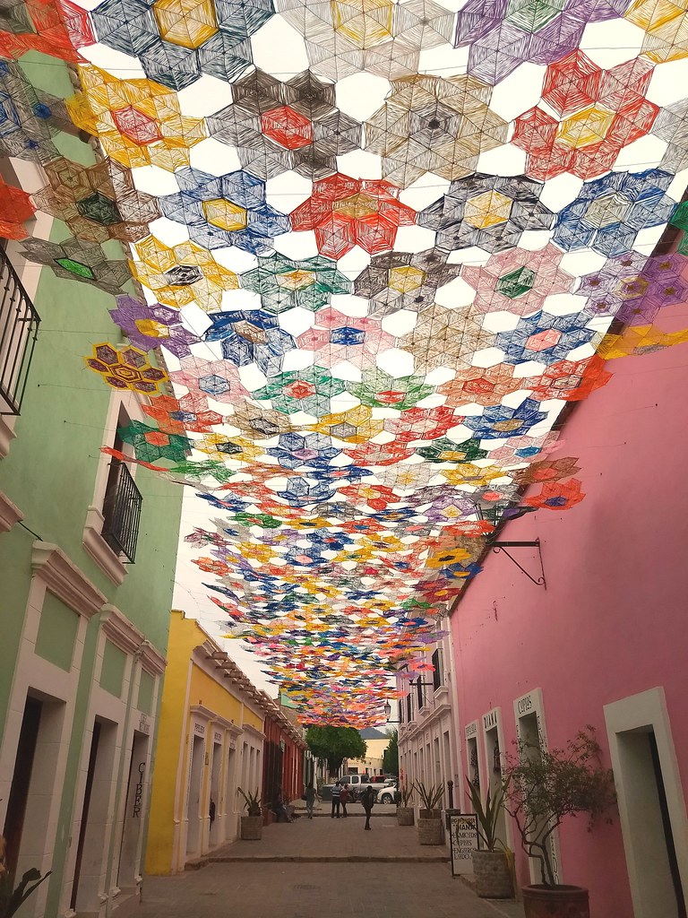 Toldo de paneles tejidos de colores sobre una calle de casas rosas y verdes, Cosalá, Sinaloa