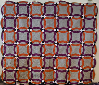 This is the project code-named 'Orangerie.' Since orange and purple were Robert and Aidan's wedding colors, I chose orange and purple shot cottons for the rings. I had to tone the grey down a couple of notches, and use a Kona solid ('pewter') to let both the orange and the purple rings have room to talk. Since Robert and Aidan are Australian, the backing is an orange-pink-purple Aboriginal print.

I had to be unusually careful about accuracy on these rings, because shot cottons do love to stretch and wobble, and those black-and-white ring intersections were absolutely unforgiving. Any inaccuracy showed. But hey, that's what pins are for.

Quilting by the always-lovely Nancy of Just Quilting PDX.