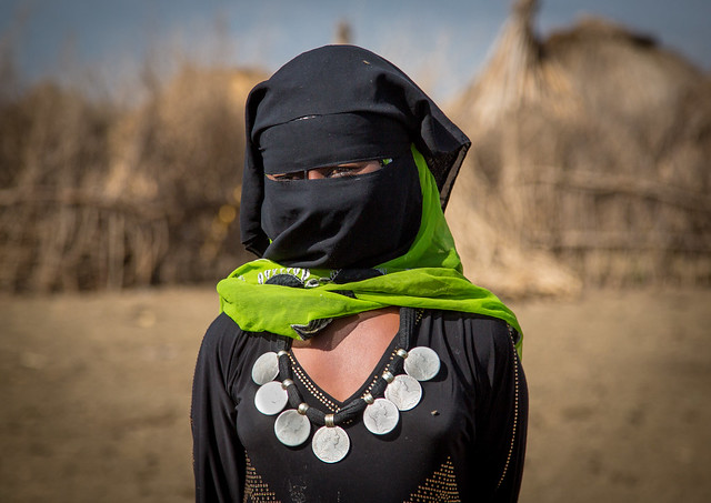 Portrait of an Oromo veiled woman with a silver thalers necklace standing in front of her village, Amhara region, Artuma, Ethiopia