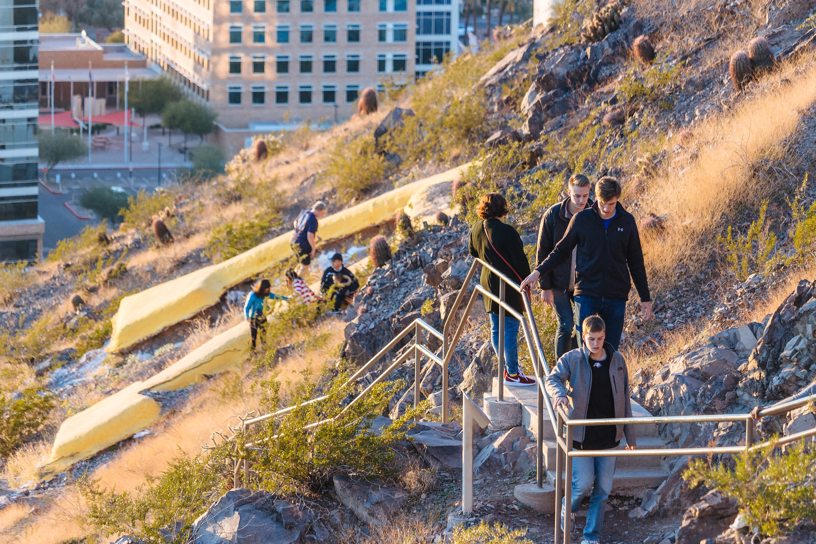 Hikers hold onto railings as they climb up the side of a mountain with a large letter A in Tempe, Arizona