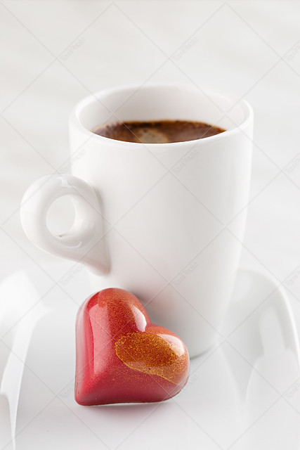 Red heart shaped handmade chocolate candy on plate with cup of coffee espresso