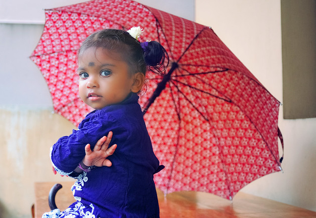 Indian baby girl under a large umbrella during the monsoon season