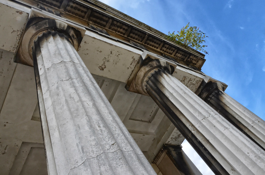 Two Doric Order columns shown from the ground up. The rood can also be seen, and there are blue skies that fill the right, top side of the photo. 