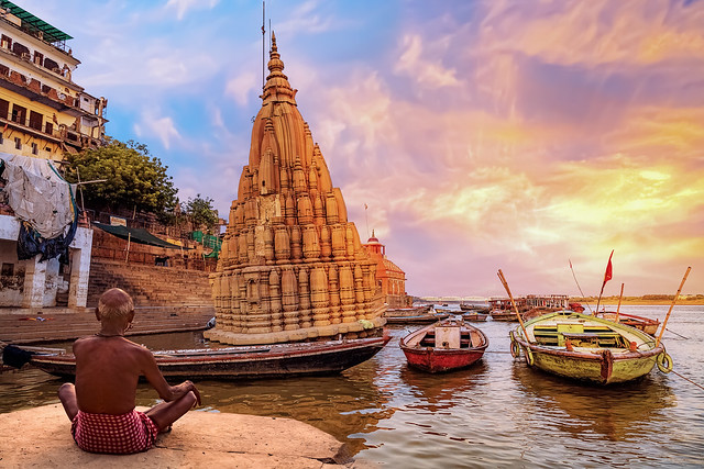 Old man meditates at Varanasi Ganges river bank at sunrise.
