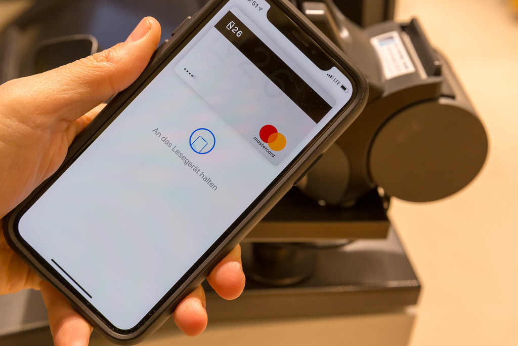 Apple Pay auf in der Hand gehaltenem Smartphone vor Kasse | Flickr