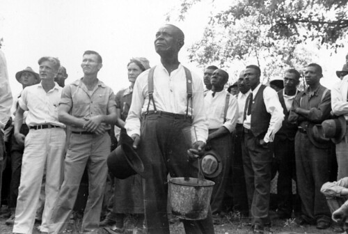 Image verso: "An early union meeting." Black and White STFU members including Myrtle Lawrence and Ben Lawrence, listen to Norman Thomas speak outside Parkin, Arkansas on September 12, 1937. One man carries an enamel pot and drinking glass.