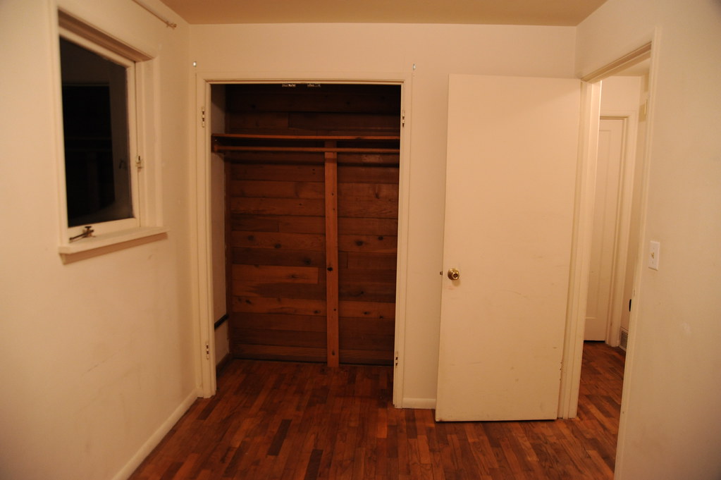 An empty bedroom on the morning of a group showing An empty bedroom with bare walls, a wood floor and an open closet with a hanging rail.