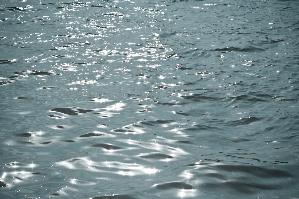 Sunlight glinting and sparkling like diamonds across the rippling surface of deep blue-gray coastal water.