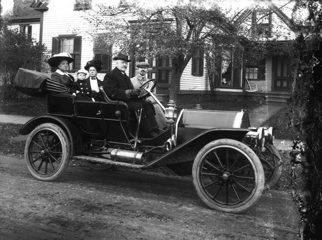 Family in old car in front of house