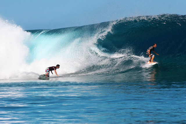 Two surfers conquering a wave at Teahupoo.