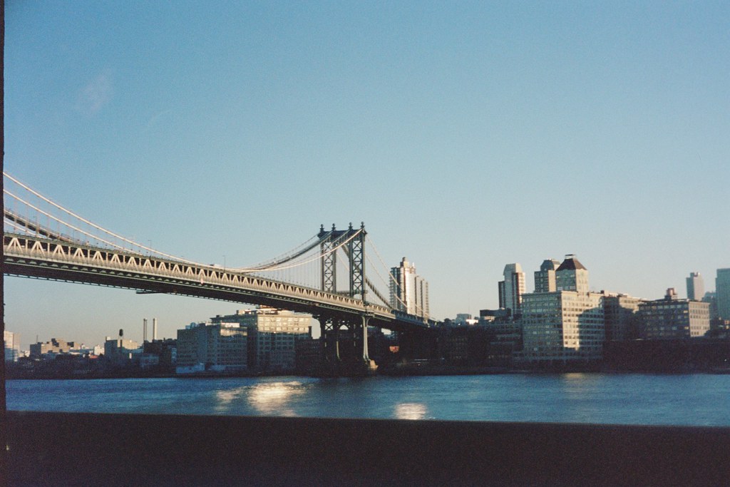 Manhattan Bridge spanning the East River with morning sun reflecting before Brooklyn waterfront.