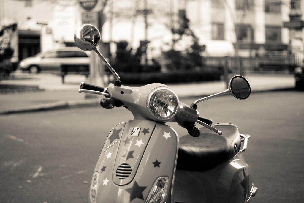Black and white photograph of a Vespa scooter decorated with star decals parked on a city street.
