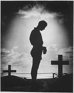 A Coast Guardsman stands in silent reverence beside the resting place of a comrade., 1944 | by The U.S. National Archives