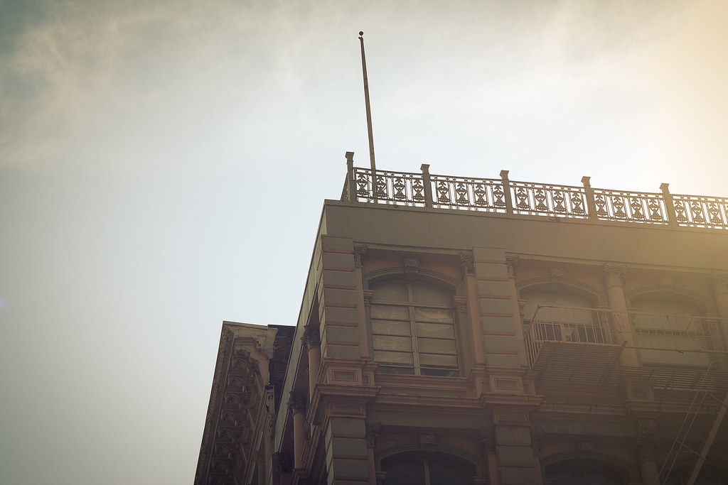 Historic cast-iron building facade with decorative rooftop balustrade and flagpole in sunlight.