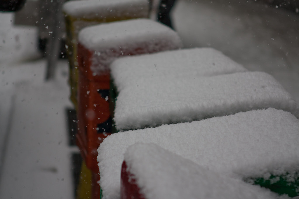 Colorful street newspaper vending boxes covered in thick pillows of freshly fallen snow.