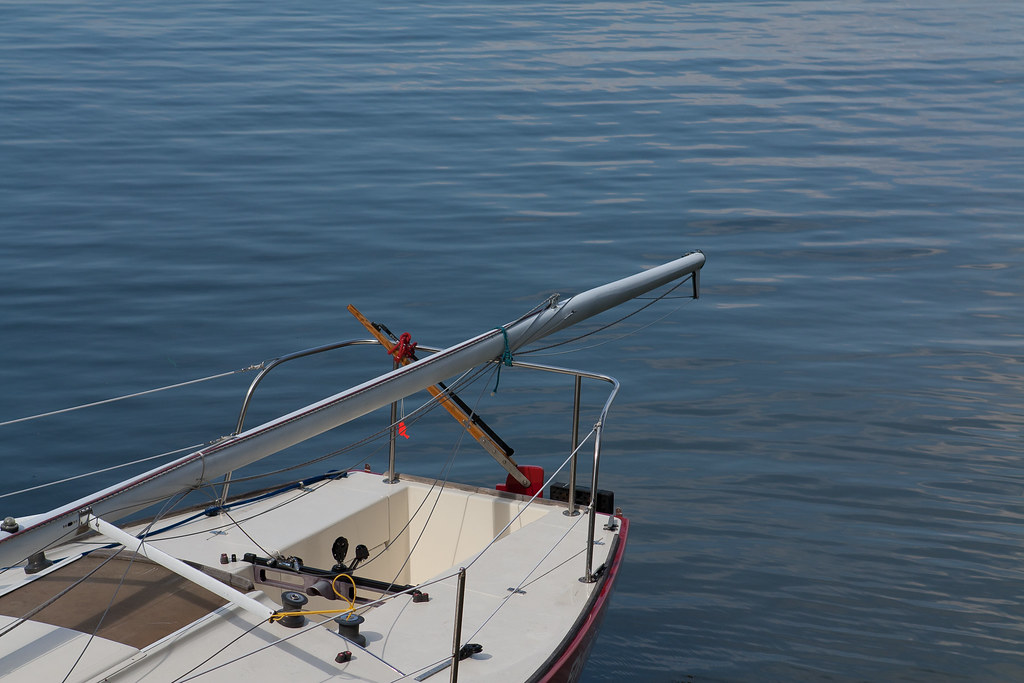 Stern and boom of a small white sailboat resting on deep blue rippling water with visible rigging.