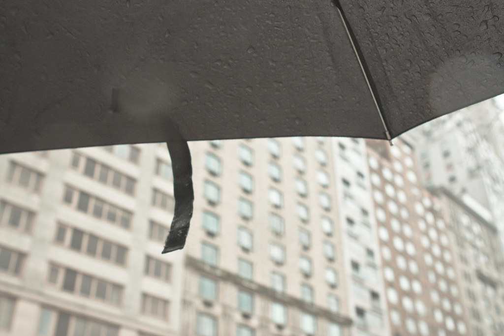 Raindrop-speckled black umbrella framing the facade of tall apartment buildings in the rain.