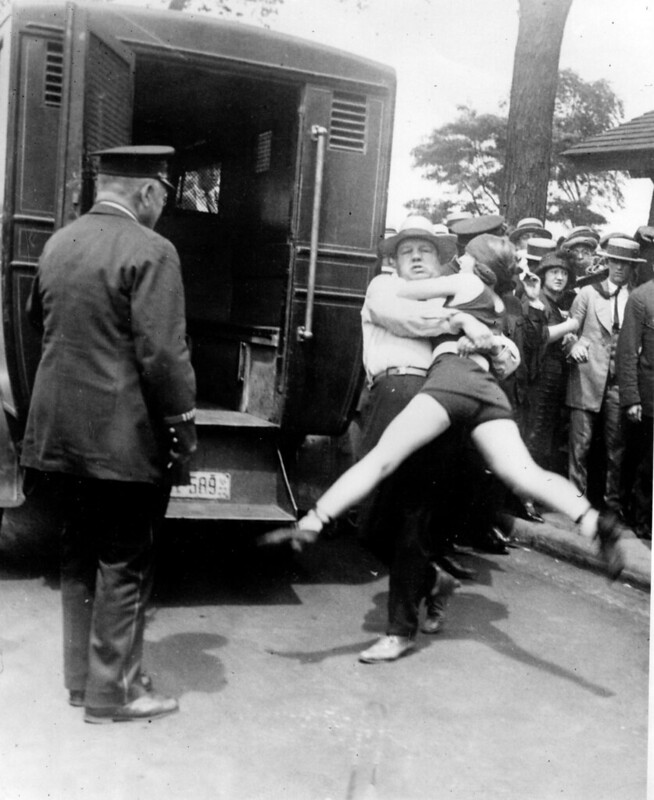 Man struggling to put a young woman in the back of a police wagon