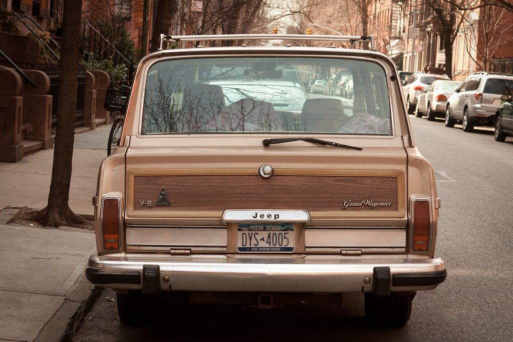 Beige Jeep Grand Wagoneer with woodgrain tailgate and NY plates parked on a brownstone street.