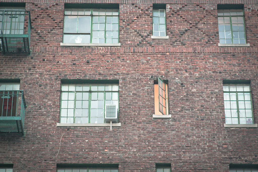 Brick building exterior with green casement windows and a single open window with warm light.