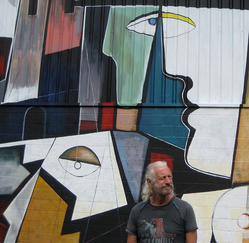Artist standing beside a wall mural of angular faces